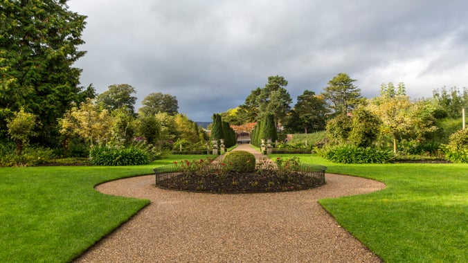 The center bedding of the Victorian garden, featuring flower beds with a variety of plants. In the distance, yew trees form a walk.